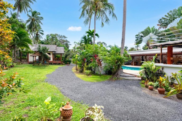 Jardín tropical con camino de grava y piscina exterior del Tropical Heavens Garden Samui