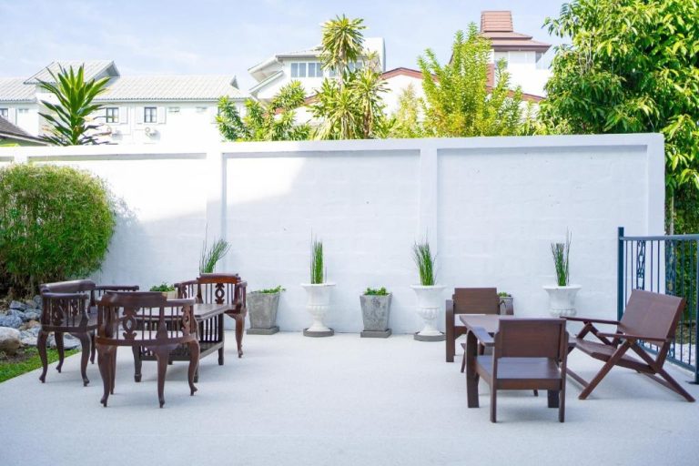 Terraza exterior con mesas y sillas de madera en el jardín del Singharaj Boutique Hotel