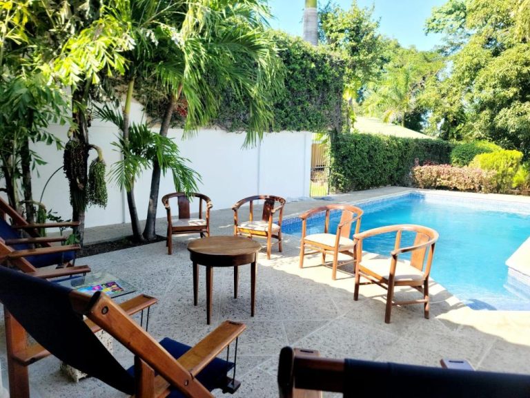 Terraza con sillas de madera junto a la piscina exterior del Hotel Casa del Sol rodeada de palmeras
