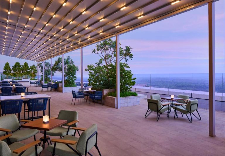 Terraza bar con vistas panorámicas al atardecer en el Taj The Trees Mumbai con mesas y jardines
