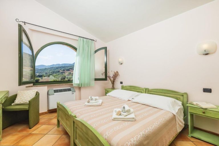 Habitación doble con camas verdes y ventana arqueada con vistas a la montaña en Hotel Janas