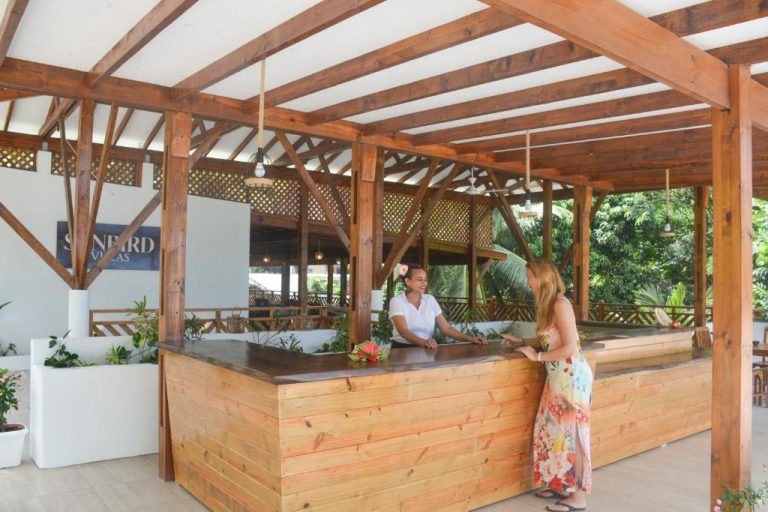 Recepción exterior de madera de Sunbird Villas con personal atendiendo a huésped en zona tropical