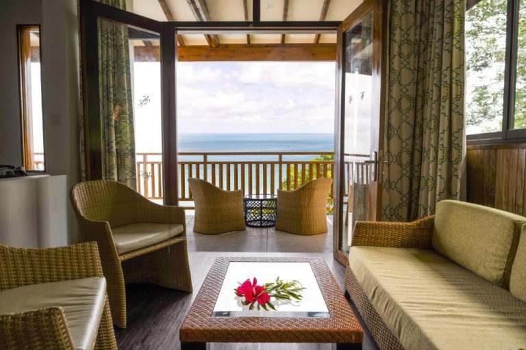 Salón con terraza y vista panorámica al mar en Sunbird Villas, con mobiliario de ratán y decoración tropical