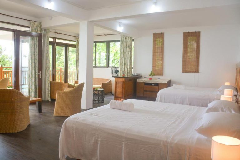Habitación espaciosa con múltiples camas blancas y terraza en Sunbird Villas