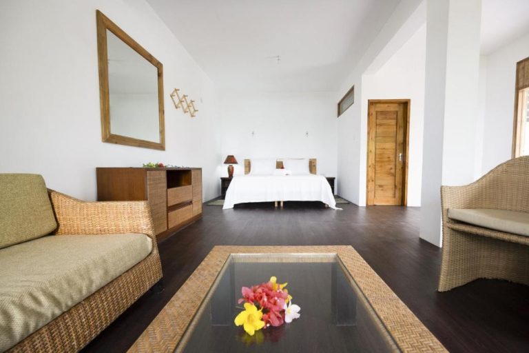 Suite amplia con salón, sofás de ratán y cama doble en Sunbird Villas con decoración tropical