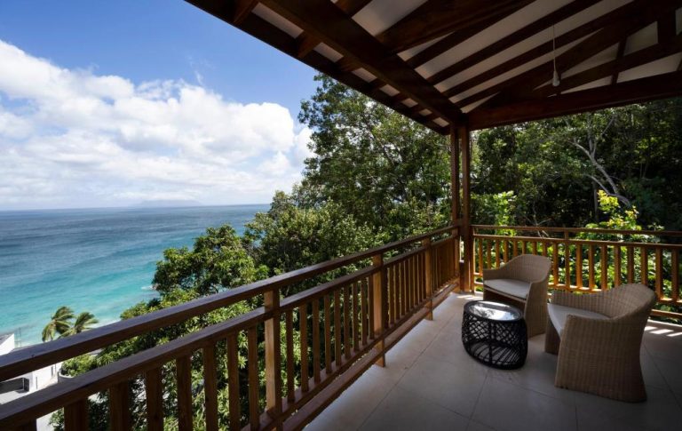 Terraza privada con sillas de ratán y vistas al mar turquesa en Sunbird Villas rodeada de vegetación