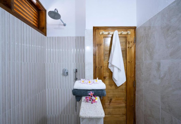 Baño con ducha de lluvia, toallas y flores tropicales en Sunbird Villas