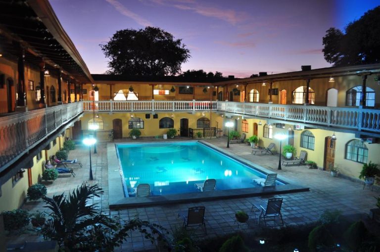 Piscina exterior iluminada del Hotel Córdoba en patio interior colonial con galería y jardines al atardecer