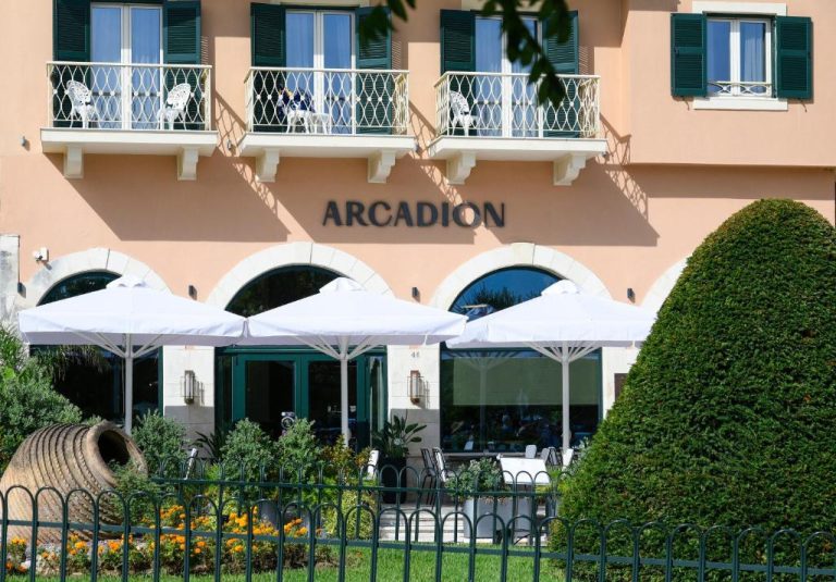 Terraza exterior con sombrillas blancas y jardín del Arcadion Hotel en Corfú