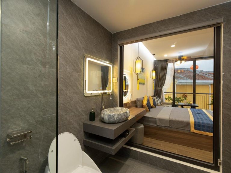 Baño de mármol con vista al dormitorio en Hai Hội Villa Hoi An, con espejo LED y lavabo de piedra natural