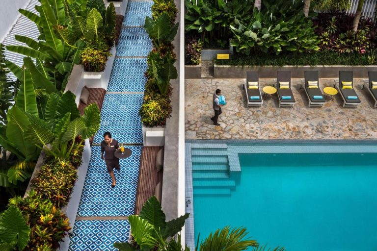 Vista aérea de la piscina exterior y jardines tropicales con personal de servicio en Viroth's Hotel