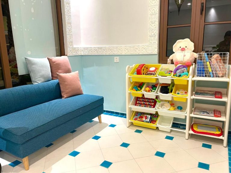 Sala de juegos infantil con estantería de juguetes y sofá azul en Mellon OASIS Phu Quoc