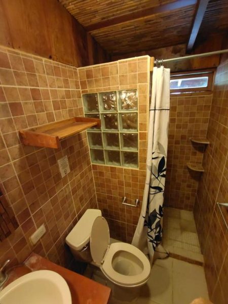 Baño rústico con ducha, bloques de vidrio y decoración en madera del hotel Coco Bay