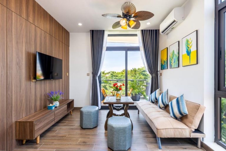 Salón moderno con sofá, TV y balcón con vistas verdes en Hai Hội Villa Hoi An