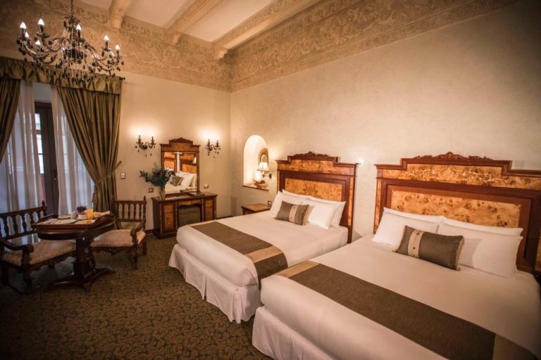 Habitación doble de estilo colonial con camas queen y araña de cristal en Aranwa Cusco Boutique Hotel