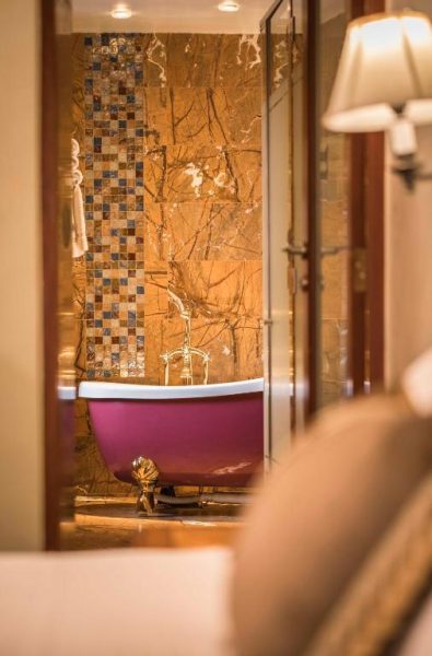 Bañera exenta rosa con griferías doradas y pared de mármol en el spa del Aranwa Cusco Boutique Hotel