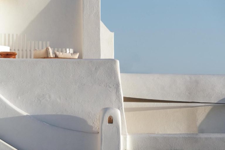 Terraza exterior de paredes blancas con cojines y vistas al mar en Belvedere Suites Santorini