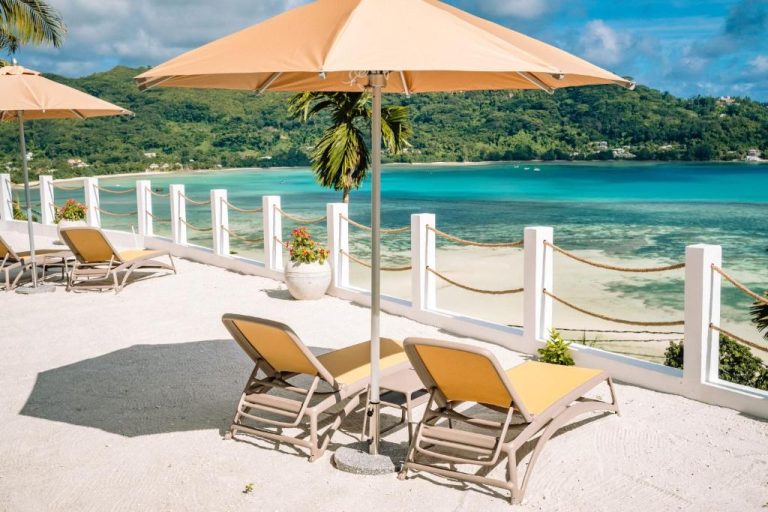 Terraza con tumbonas y sombrillas frente al mar turquesa en The Bay Seychelles Boutique Hotel