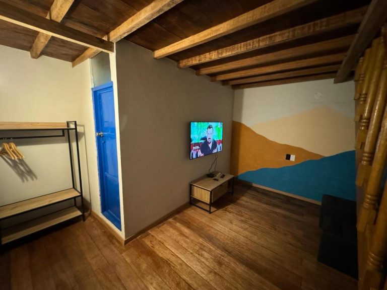 Habitación con TV en pared, mural decorativo de montañas y techo de vigas de madera en Way Kap Hostel Cusco