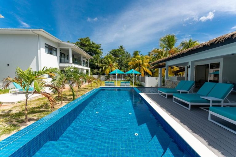 Piscina exterior con tumbonas azules y palmeras en Anse La Mouche Villas, Seychelles