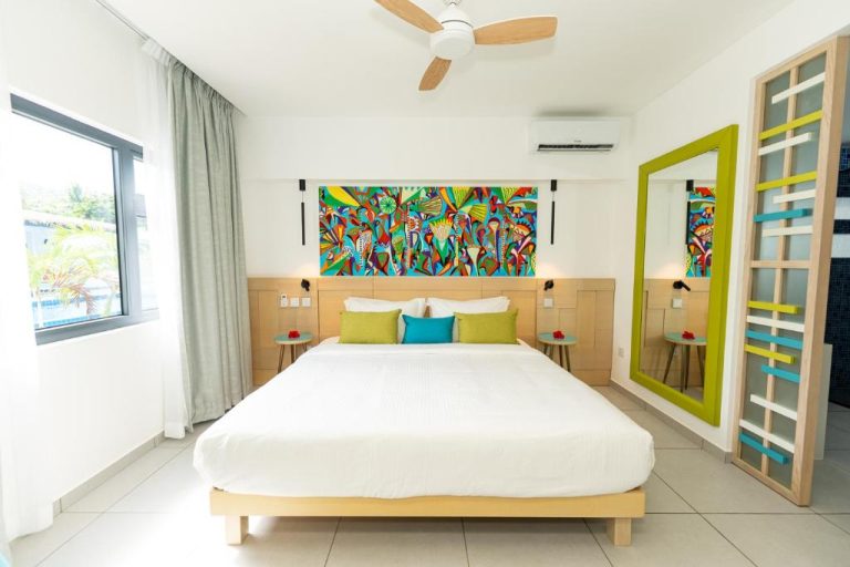 Habitación doble con decoración tropical y colorida en Anse La Mouche Villas, con cama king y arte vibrante