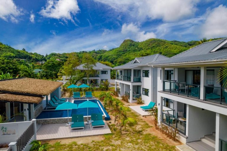 Piscina exterior con tumbonas y sombrillas turquesas en Anse La Mouche Villas rodeada de montañas