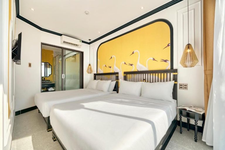 Habitación doble con mural de cisnes en amarillo y camas blancas del Rokas Hoi An Boutique Hotel