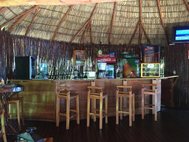Bar de palapa tropical con taburetes de madera y neveras de Coca-Cola y Toña en Laguna Beach Club
