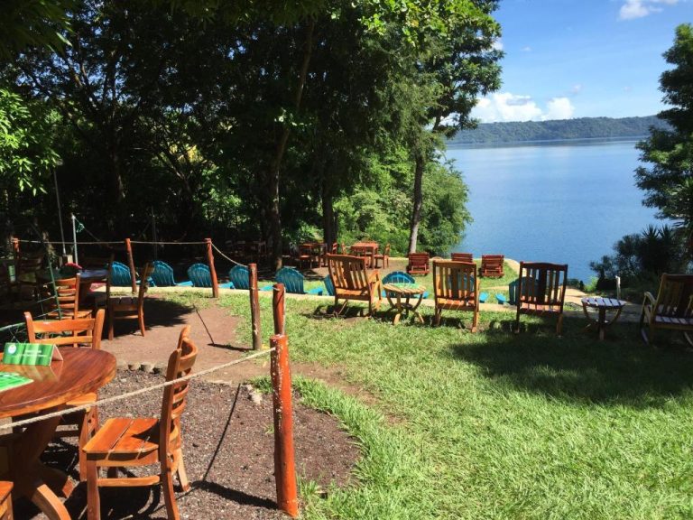 Terraza exterior con sillas y mesas de madera en Laguna Beach Club con vistas al lago rodeado de naturaleza
