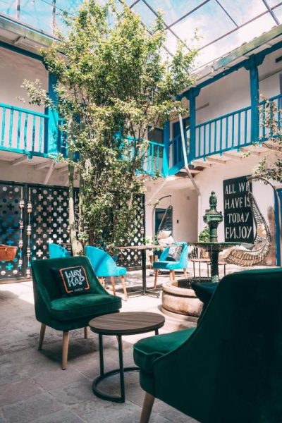 Patio interior con sillones verdes y balcones azules del Way Kap Hostel Cusco