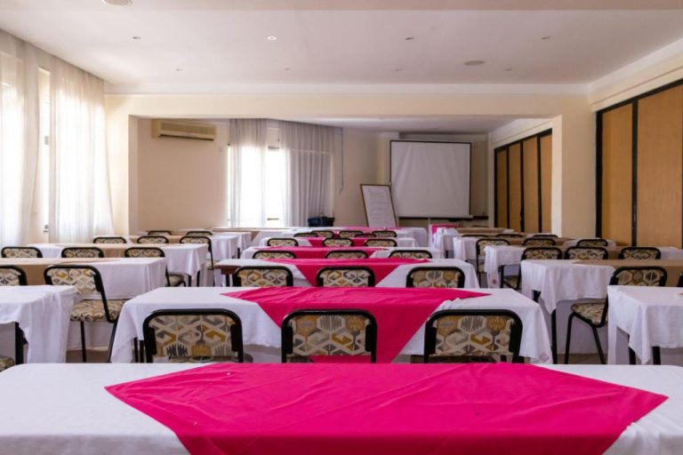 Sala de conferencias del Royal Court Hotel con mesas en disposición escalonada y pantalla de proyección