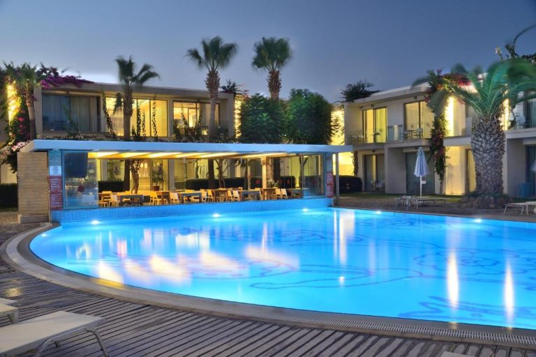 Piscina exterior iluminada del Lugga Boutique Hotel & Beach con restaurante y palmeras al atardecer