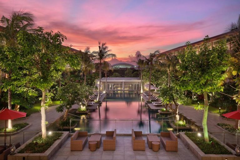 Piscina exterior iluminada al atardecer del Hilton Garden Inn Bali Ngurah Rai Airport con jardines tropicales