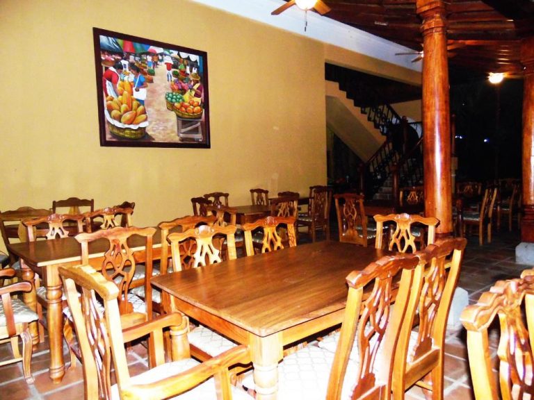 Restaurante del Hotel Córdoba con mesas y sillas de madera tallada y cuadro de mercado típico en la pared