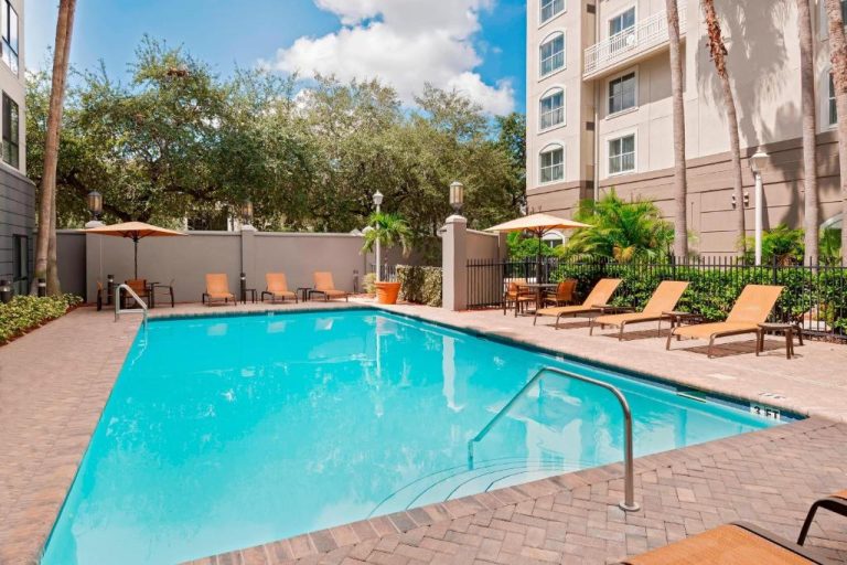 Piscina exterior con tumbonas y sombrillas del Residence Inn Tampa Downtown rodeada de palmeras