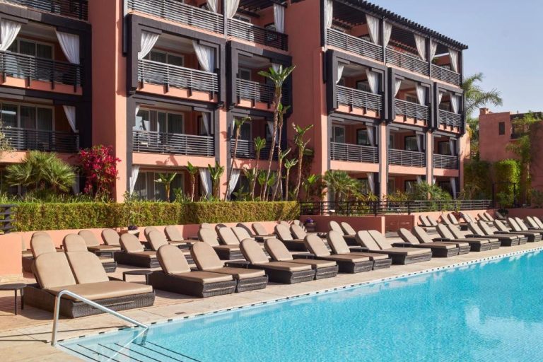 Piscina exterior con tumbonas y vistas a la fachada del Hôtel Barrière Le Naoura en Marrakech