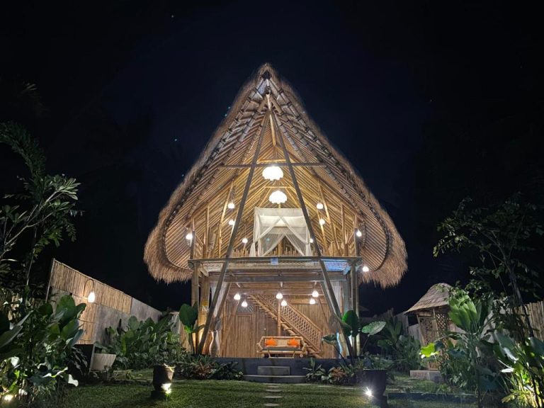 Cabaña de bambú iluminada por la noche en Pitu a Punggul Village Escape con techo de paja triangular