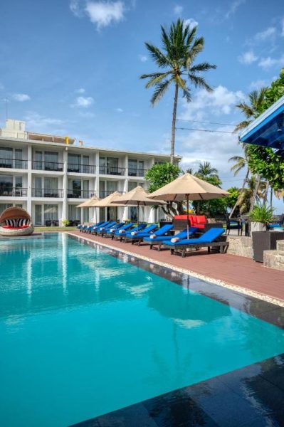 Piscina exterior con tumbonas azules y palmeras del Camelot Beach Hotel en Sri Lanka