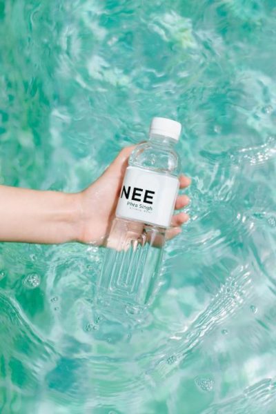 Botella de agua mineral del hotel Nanee Phra Singh sostenida sobre una piscina de aguas turquesas