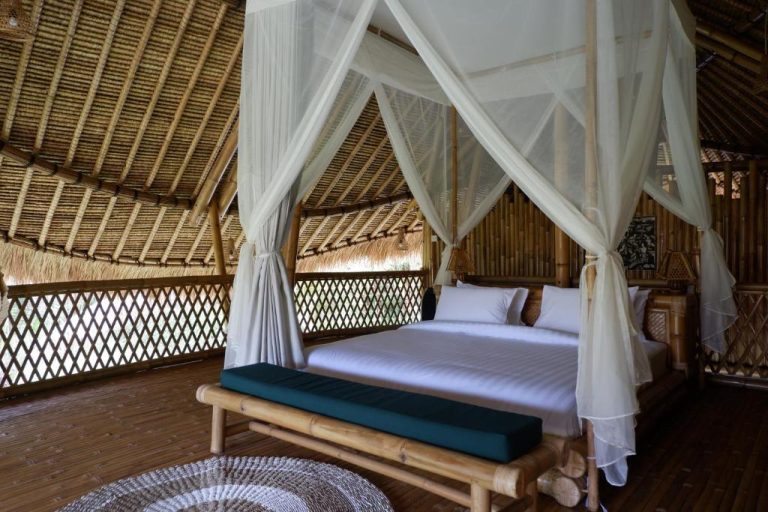 Habitación con cama de dosel y mosquitera en cabaña de bambú del Pitu Punggul Village Escape Bali
