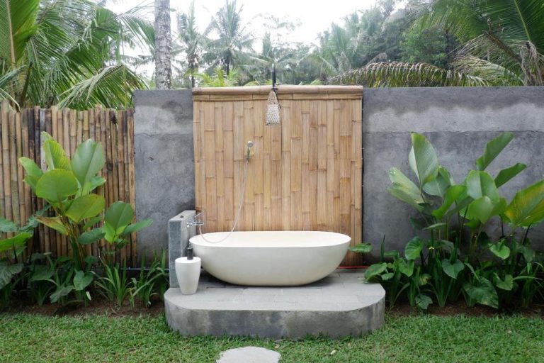 Bañera exterior de piedra en jardín tropical con bambú del hotel Pitu Punggul Village Escape en Bali