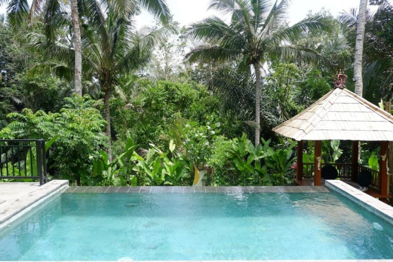 Piscina infinita rodeada de vegetación tropical y gazebo balinés en Pitu Punggul Village Escape