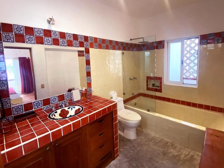 Baño con azulejos de talavera roja, tina y ducha del Zihil Ha Hotel