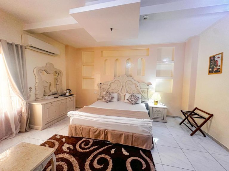 Habitación doble con cama matrimonial y cabecero ornamental blanco en el Riyam Hotel