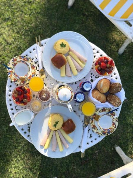 Desayuno completo servido en mesa de jardín en CasaIvan con embutidos, frutas y zumo de naranja