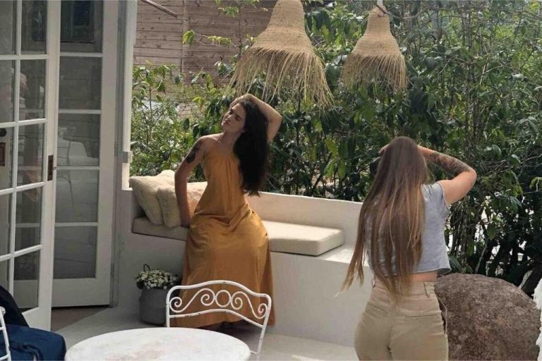 Terraza exterior de CasaIvan con mujer posando en vestido dorado entre lámparas de rafia y vegetación