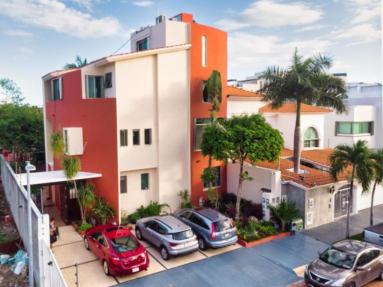 Fachada exterior del Humant Coliving Cancún con estacionamiento privado, palmeras y arquitectura moderna