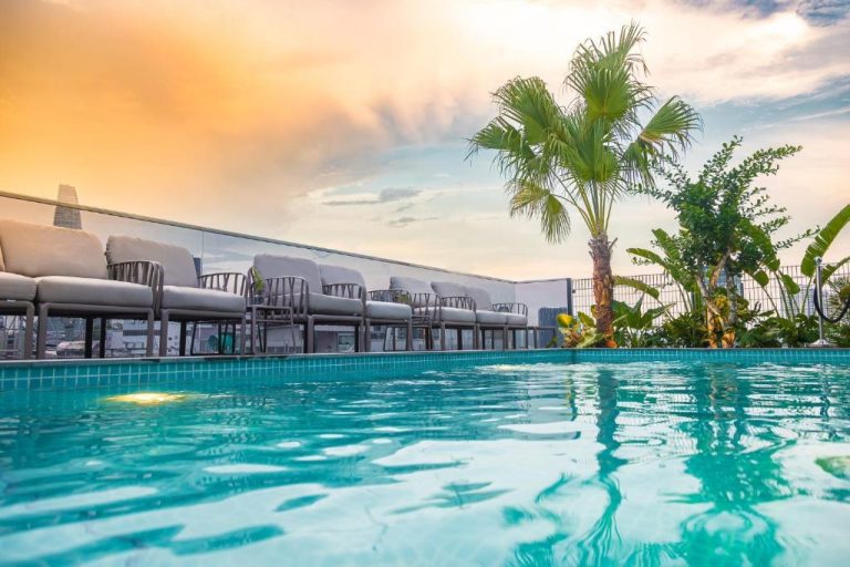 Piscina en la azotea con tumbonas y palmeras al atardecer en La Siesta Premium Saigon Central