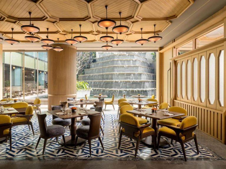Elegante restaurante interior del Dusit Thani Bangkok con sillas amarillas, techo octagonal y cascada exterior