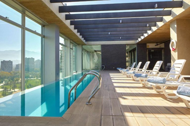 Piscina interior con tumbonas y vistas panorámicas de Santiago en Radisson Blu Plaza El Bosque